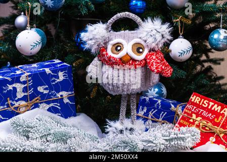 Weiche, weiche Spielzeugeule mit Kopfhörern und Strickschal. Wintergeschenk für Kinder. Lustige rot-weiße gestrickte Toy-Eule mit rotem Hut und großen Augen Stockfoto