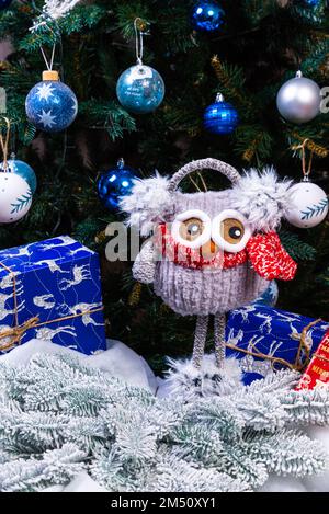 Weiche, weiche Spielzeugeule mit Kopfhörern und Strickschal. Wintergeschenk für Kinder. Lustige rot-weiße gestrickte Toy-Eule mit rotem Hut und großen Augen Stockfoto