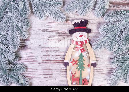 Weihnachtsdekorationen vor verschwommenem Hintergrund. Kleiner Schneemann aus Holz. Rustikale Schneeflocke aus Holz. Nahaufnahme eines glücklichen Schneemanns, der lächelt Stockfoto