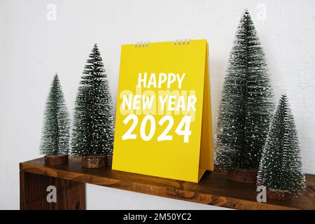 Frohes neues Jahr 2024 Textnachricht mit weihnachtlicher Kiefernbaumdekoration auf Holzregalen Stockfoto