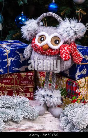 Weiche, weiche Spielzeugeule mit Kopfhörern und Strickschal. Wintergeschenk für Kinder. Lustige rot-weiße gestrickte Toy-Eule mit rotem Hut und großen Augen Stockfoto