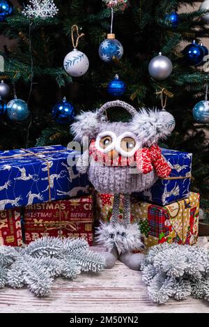 Weiche, weiche Spielzeugeule mit Kopfhörern und Strickschal. Wintergeschenk für Kinder. Lustige rot-weiße gestrickte Toy-Eule mit rotem Hut und großen Augen Stockfoto