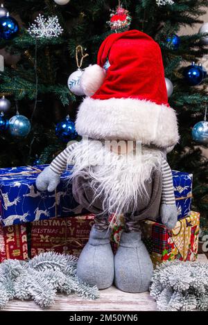 Weihnachtselfen-Dekoration. Vier Zwerge mit Weihnachtsgeschenk sitzen auf einem Holzregal. Weihnachtskonzept und Neujahrskonzept, Grußkarte Stockfoto