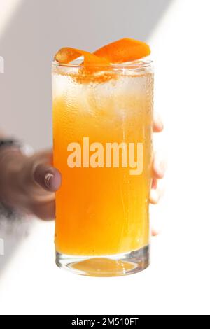 Kalter Sommercocktail in der Hand der Frau, Nahaufnahme. Die Hand einer Frau hält in einem Sommerkaffee ein beschlagenes Glas eines erfrischenden Cocktails mit Zitrone und Eis. Stockfoto