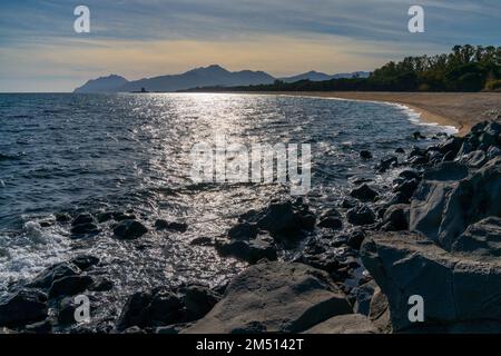 Ein Blick auf den goldenen Sandstrand in Barisardo mit dem Wachturm Torre di Bari im fernen Hintergrund Stockfoto