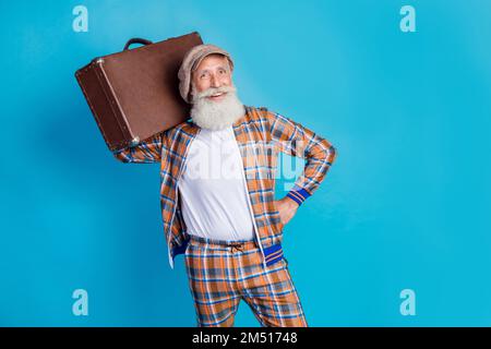 Foto eines flippigen, selbstbewussten Rentners in einem karierten Anzug, der den Koffer leer hält, isolierter blauer Hintergrund Stockfoto