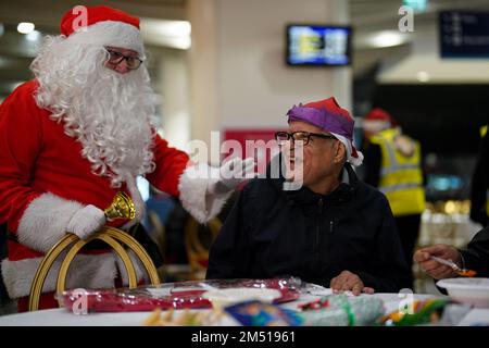 Ein als Weihnachtsmann verkleideter Mann spricht mit einem Teilnehmer beim Weihnachtsessen der Midland Langar Seva Society für Obdachlose, das in New Street Station, Birmingham, stattfindet. Freiwillige servieren ein warmes Abendessen für bis zu 250 Obdachlose und verwundbare Menschen, zusammen mit Musik, Geschenkspenden und Tanz. Foto: Samstag, 24. Dezember 2022. Stockfoto