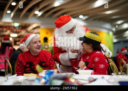 Ein als Weihnachtsmann verkleideter Mann spricht mit zwei Teilnehmern beim Weihnachtsessen der Midland Langar Seva Society für Obdachlose, das in New Street Station, Birmingham, stattfindet. Freiwillige servieren ein warmes Abendessen für bis zu 250 Obdachlose und verwundbare Menschen, zusammen mit Musik, Geschenkspenden und Tanz. Foto: Samstag, 24. Dezember 2022. Stockfoto