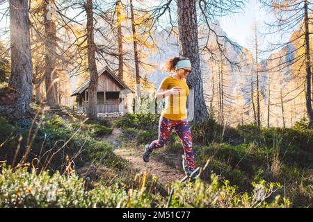 Fröhliche weiße Frau auf einer Wanderung, die durch den Herbstwald läuft, Sonnenstrahlen in den Bäumen Stockfoto