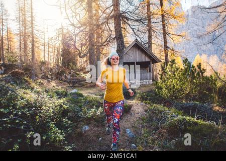 Lächelnde Wanderin mit Sonnenbrille, die an einem sonnigen Tag durch den Herbstwald läuft Stockfoto