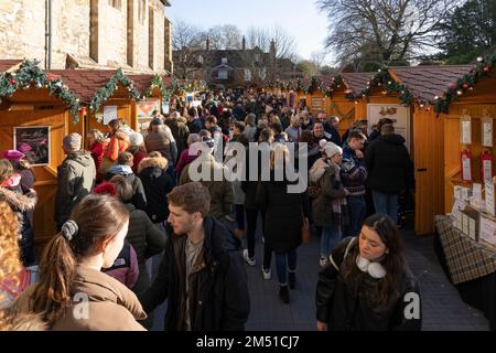 Weihnachtseinkäufer auf dem Winchester Weihnachtsmarkt mit hölzernen Chalets neben den mittelalterlichen historischen Mauern der gotischen Winchester Cathedral, England, Großbritannien Stockfoto