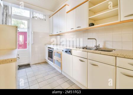 Eine Küche mit weißen Schränken und Geräten auf der Arbeitsfläche vor dem Ofen, Waschbecken und Geschirrspüler Stockfoto