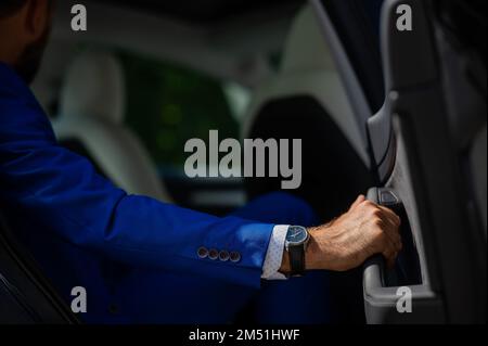 Ein Mann im blauen Anzug öffnet die Autotür. Nahaufnahme eines Mannes Hand mit einer teuren Uhr. Stockfoto