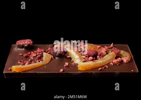 Schokoladenriegel mit kandierten Orangenschalen und Himbeeren isoliert auf schwarzem Hintergrund Stockfoto