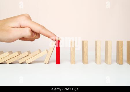 Der Domino fällt und der Finger stoppt die Kettenreaktion. Das Konzept der Problemlösung. Stockfoto