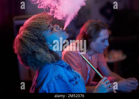 Seitenansicht der jungen Schwarzen, die Hookah-Rauch ausatmet Stockfoto