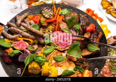 Gemischtes Fleisch und Gemüse, in einem Wok gebraten, auf einer Schüssel mit heißen Kohlen auf dem Tisch, um lange Zeit heiß zu bleiben. Stockfoto