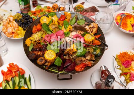 Gemischtes Fleisch und Gemüse, in einem Wok gebraten, auf einer Schüssel mit heißen Kohlen auf dem Tisch, um lange Zeit heiß zu bleiben. Stockfoto