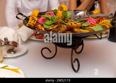 Gemischtes Fleisch und Gemüse, in einem Wok gebraten, auf einer Schüssel mit heißen Kohlen auf dem Tisch, um lange Zeit heiß zu bleiben. Stockfoto