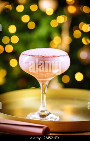 Cocktailgetränk mit Espresso-Kaffee in einem Coupé-Glas auf einem goldenen Tablett. Weihnachtsdekoration mit Lichtern im Hintergrund. Silvesterparty-Atmosphäre. Stockfoto