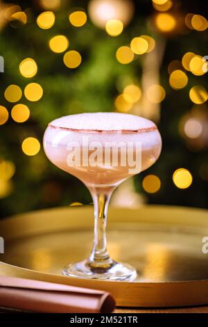 Cocktailgetränk mit Espresso-Kaffee in einem Coupé-Glas auf einem goldenen Tablett. Weihnachtsdekoration mit Lichtern im Hintergrund. Silvesterparty-Atmosphäre. Stockfoto