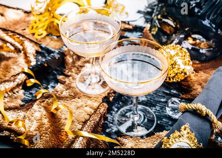 Zwei Gläser Sekt auf einem festlichen Tisch für Silvester, Party oder Karneval in goldenem und schwarzem Ton Stockfoto