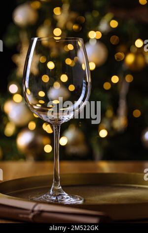 Leeres elegantes Weinglas vor dem Weihnachtsbaum mit Lichtern für Silvesterparty im Hintergrund Stockfoto