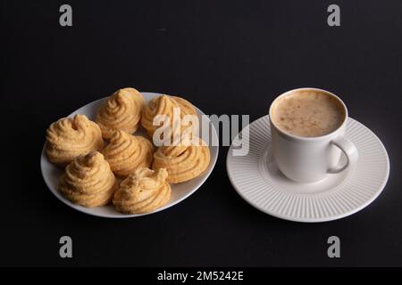 Foto von mehreren Baiser-Kuchen auf einem Teller und einer Tasse Kaffee, die nebeneinander auf schwarzem Hintergrund stehen Stockfoto