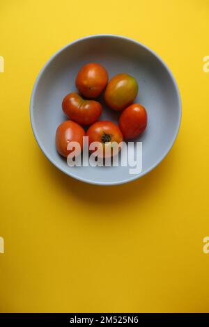 Hausgemachte Tomaten in verschiedenen Farben Rot-Gelb-Orange liegen auf einer grauen Platte auf gelbem Hintergrund mit einem Platz für Text-Copyspace. Seitenansicht von Stockfoto