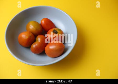 Hausgemachte Tomaten in verschiedenen Farben Rot-Gelb-Orange liegen auf einer grauen Platte auf gelbem Hintergrund mit einem Platz für Text-Copyspace. Seitenansicht von Stockfoto