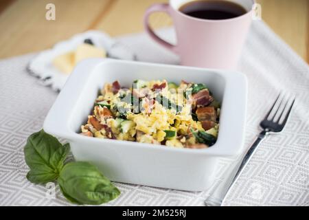 Eine Nahaufnahme des gut aussehenden Frühstücksauflaufs in der weißen Schüssel neben einer Tasse Kaffee und Scheiben Butter Stockfoto