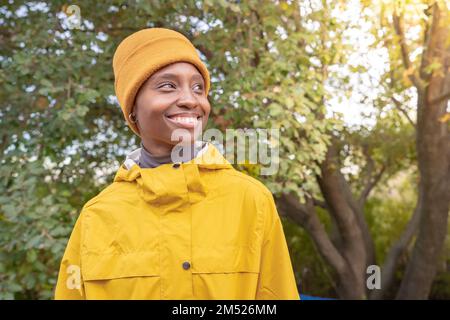 Junge Frau mit gelber Mütze, die lacht, während sie an einem sonnigen Wintertag draußen in einem Park steht Stockfoto