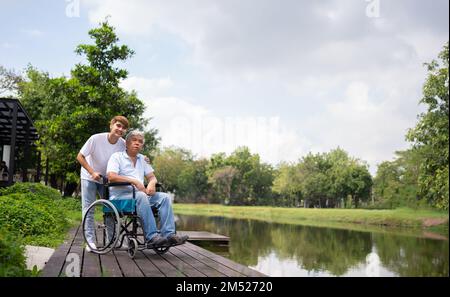 Asiatische sorgfältige Pflegekraft oder Krankenschwester halten die Hand des Patienten und ermutigen den Patienten in einem Rollstuhl. Konzept der glücklichen Ruhestand mit Pflege aus einer caregiv Stockfoto