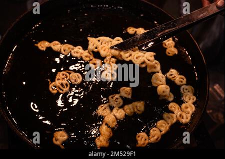 Tehatta, Westbengalen, Indien. 23. Dezember 2022. Jalebi ist ein sehr beliebter süßer Snack in Süd- und Westasien, Afrika und Mauritius. Es gibt viele Namen, einschließlich Jilapi, Zelepi, Jilebi, Jilipi, Zulbia, jerry, Mushabak, z'Labia oder Zalabia. Die südasiatische Sorte wird durch Frittieren von maida-Mehlteig (einfaches Mehl oder Allzweckmehl) in Brezel- oder Kreisform hergestellt, der dann in Zuckersirup getränkt wird. Jalebi wird mit Quark oder Rabri (in Nordindien) zusammen mit optionalen anderen Geschmacksrichtungen wie Kewra (duftendes Wasser) gegessen. Dieses Foto wurde auf einem Dorfmarkt gemacht, wo heiße Jalebi-s waren Stockfoto