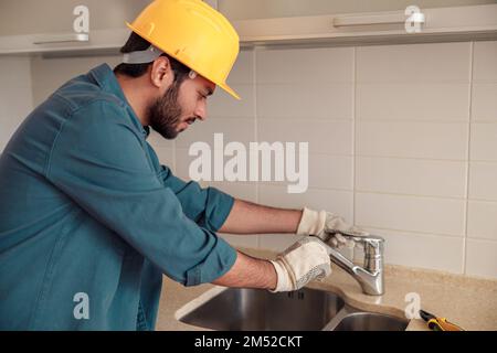 Männlicher Klempner repariert Wasserhahn in der Kundenküche. Guter Service für die Sanitäranlagen Stockfoto