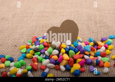 Herz aus Papier inmitten der bunten Steinchen auf Leinwand Boden Stockfoto