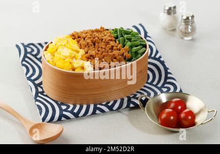 Sanshoku Lunchbox mit dreifarbigem japanischem Reis und gebratenem Hähnchen, gekochten französischen Bohnen und Rühreiern. Stockfoto