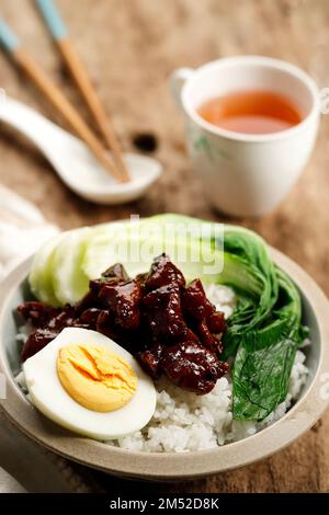 Nahaufnahme von geschmortem taiwanesischem Schweinefleisch über Reis mit halb gekochtem GGG und Pak Choi. Auf Einem Holztisch Stockfoto