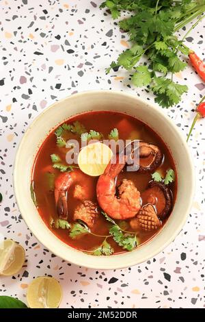 Top View Tom Yum Gung mit Garnelen, Tintenfisch und Pilz. Serviert mit Korriander und Limette Stockfoto