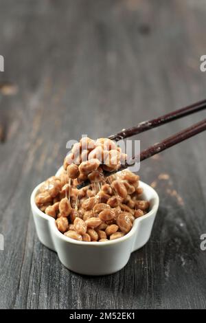 Natto wurde mit Chopstick angehoben. Natto ist eine japanische fermentierte klebrige Sojabohnen mit Stinky-Geruch. Auf Einem Holztisch Stockfoto