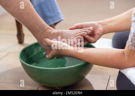Die weibliche Pflegekraft wischt die Füße der älteren Frau mit einem Handtuch ab. Stockfoto