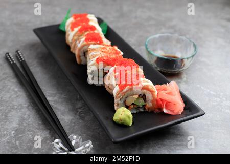 Sushi-Lachsrolle mit Avocado, Gurke auf schwarzem Teller, Nahaufnahme Stockfoto
