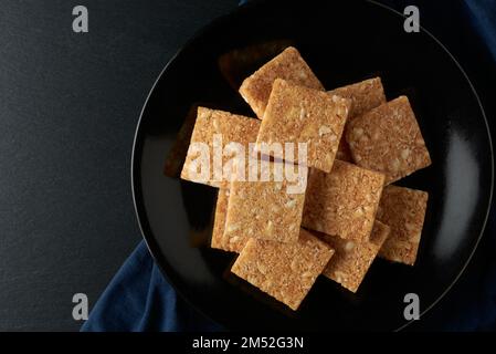 Kokosnusskekse auf schwarzem Teller, strukturierte, knusprige, quadratische, hausgemachte Kekse auf einem Tisch, von oben genommen mit Platz für Kopien Stockfoto