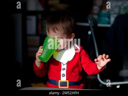 Porträt eines süßen kleinen Jungen in Weihnachtsmannkleidung, der Wasser aus dem grünen Glas trinkt Stockfoto