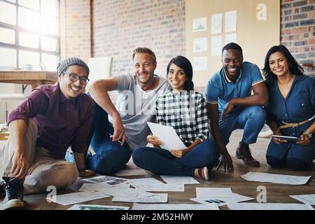 Überlassen Sie es uns als innovative Denker. Porträt einer Gruppe von Geschäftsleuten, die in einem Büro auf dem Boden Brainstorming betreiben. Stockfoto