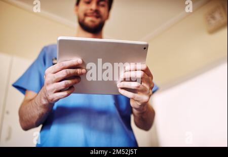 Er teilte einige Forschungen mit der medizinischen Gemeinschaft. Ein glücklicher junger Arzt, der sein Tablet in seiner Praxis benutzt. Stockfoto