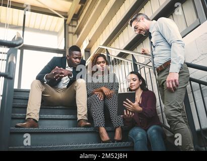 Neue Räume bedeuten neue Ideen. Eine vielfältige Gruppe von Kollegen, die ein spontanes Meeting mit einem Tablet auf der Treppe abhalten. Stockfoto