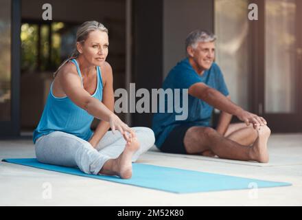 Dehnübungen sind immer wichtig. Ein reifes und glückliches Paar, das sich streckt, bevor es außerhalb seines Zuhauses Yoga macht. Stockfoto
