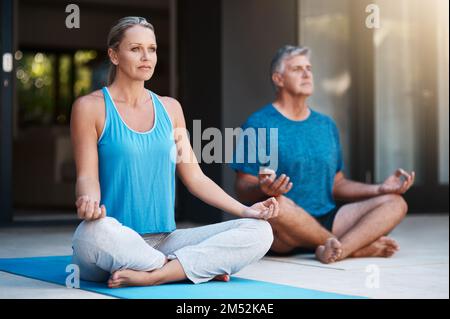 Ich versuche, eine Verbindung zu unseren inneren Wesen herzustellen. Ein reifes und glückliches Paar, das morgens vor ihrem Haus meditiert. Stockfoto