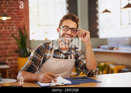 Ich bin ein Champion bei der Verwaltung. Porträt eines glücklichen jungen Geschäftsbesitzers, der an einem Tisch in seinem Café als Verwalter tätig ist. Stockfoto